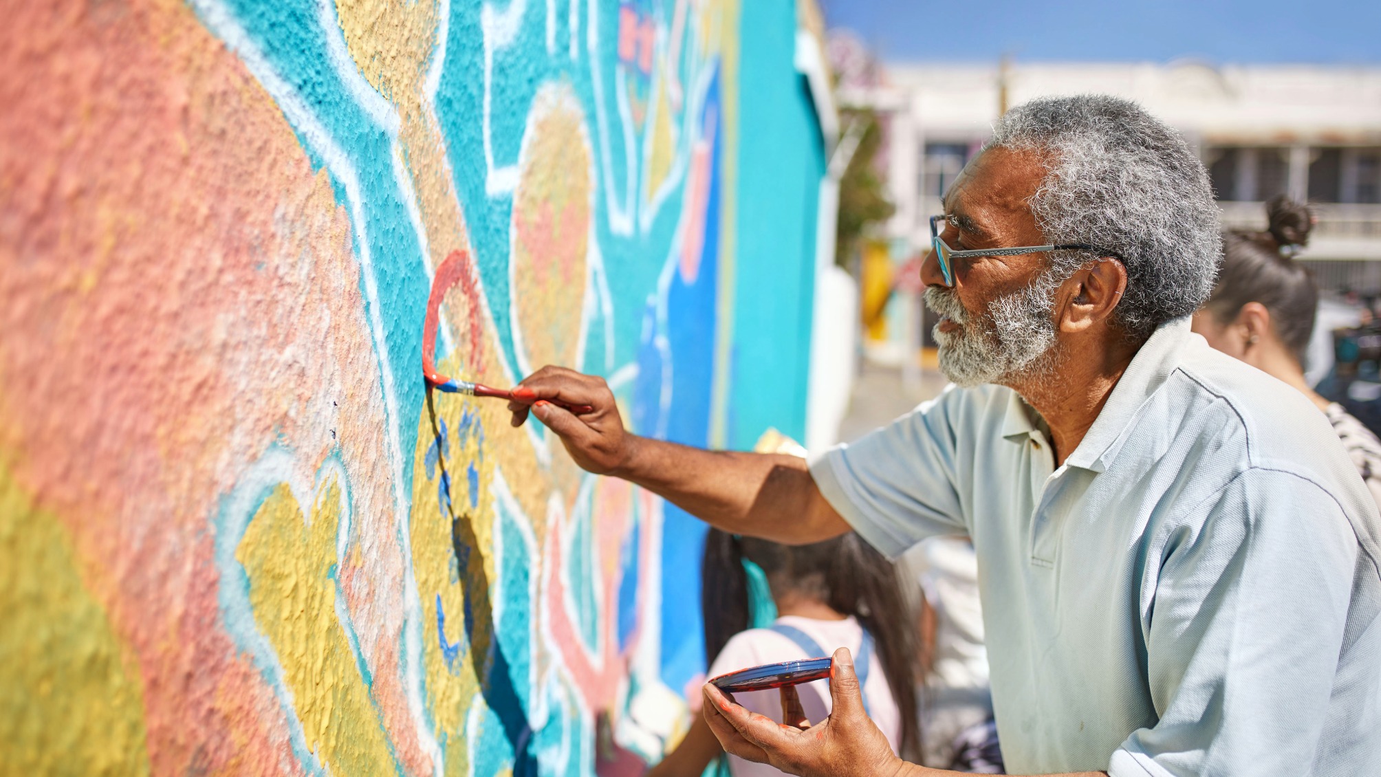 Senior male volunteer painting vibrant mural on sunny wall