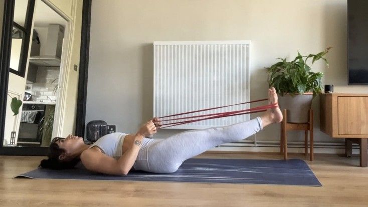 Writer Sam performing banded leg raises with legs extended just above the floor during workout at home