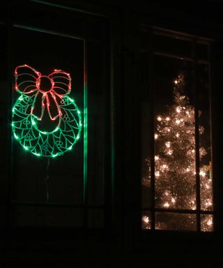 neon wreath light in christmas window alongside faux tree