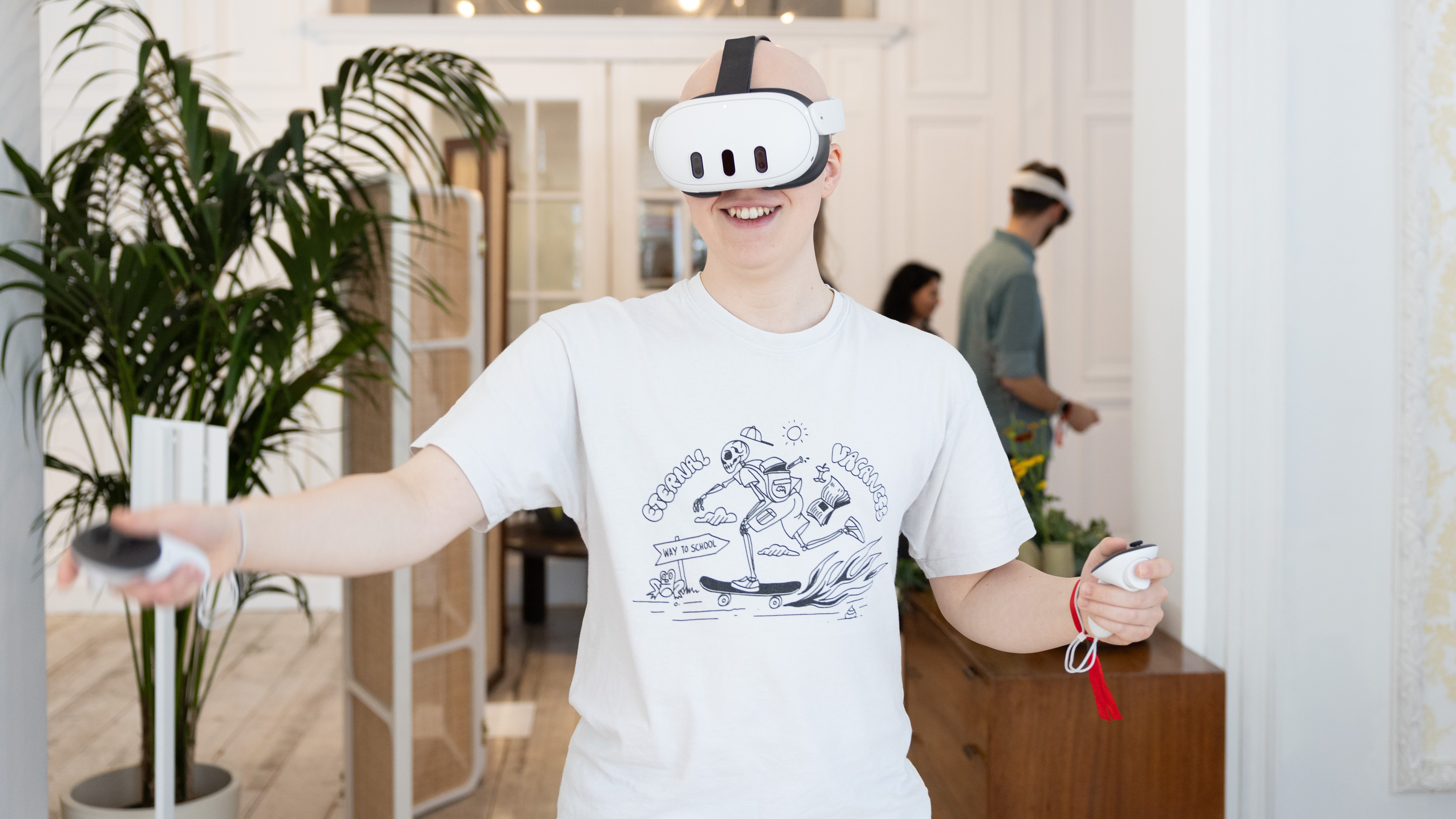 Хэмиш улыбается играя в VR-игру с помощью Meta Quest 3, он стоит перед растением в большом пространстве, похожем на гостиную