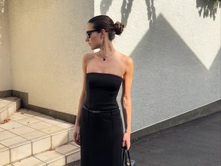 Illirida poses in black tube dress with column-like skirt, heels, and a handbag.