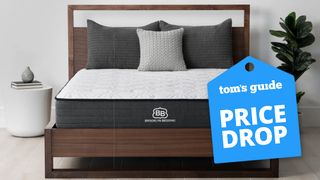 A Brooklyn Bedding Essentials mattress in a bedroom, a Tom's Guide price drop deals graphic (right)