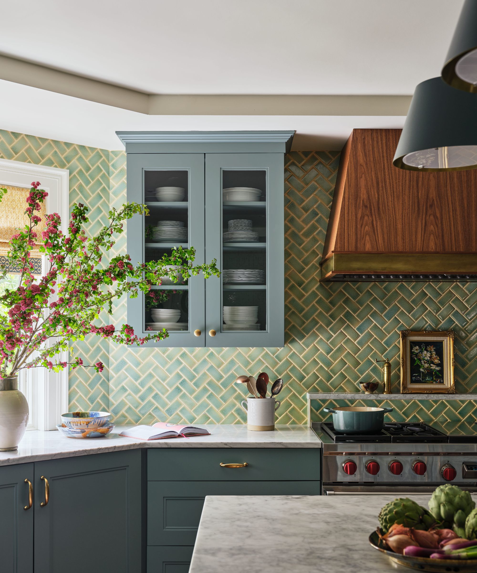 Kitchen corner with dark blue-green cabinets, green herringbone tile backsplash, and a wooden vent hood over the stove.