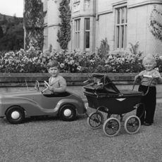 King Charles and Princess Anne playing with a toy car and buggy as kids