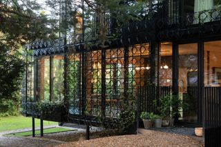 A house with black metal latticework surrounded by woodlands