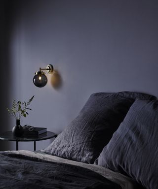 An example of how to plan bedroom lighting showing a dark grey wall with a black spherical wall light behind a dark grey bed