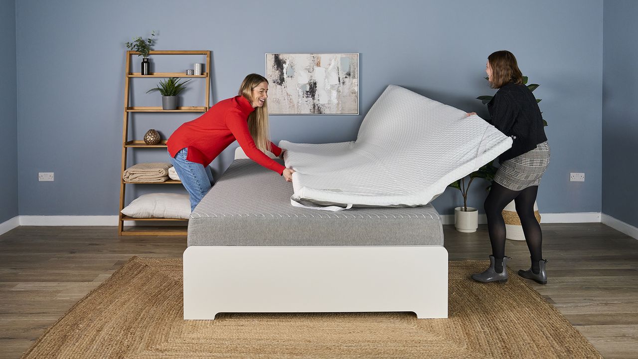 Testers unfold the unboxed Helix Dual Comfort Mattress Topper on a bed.