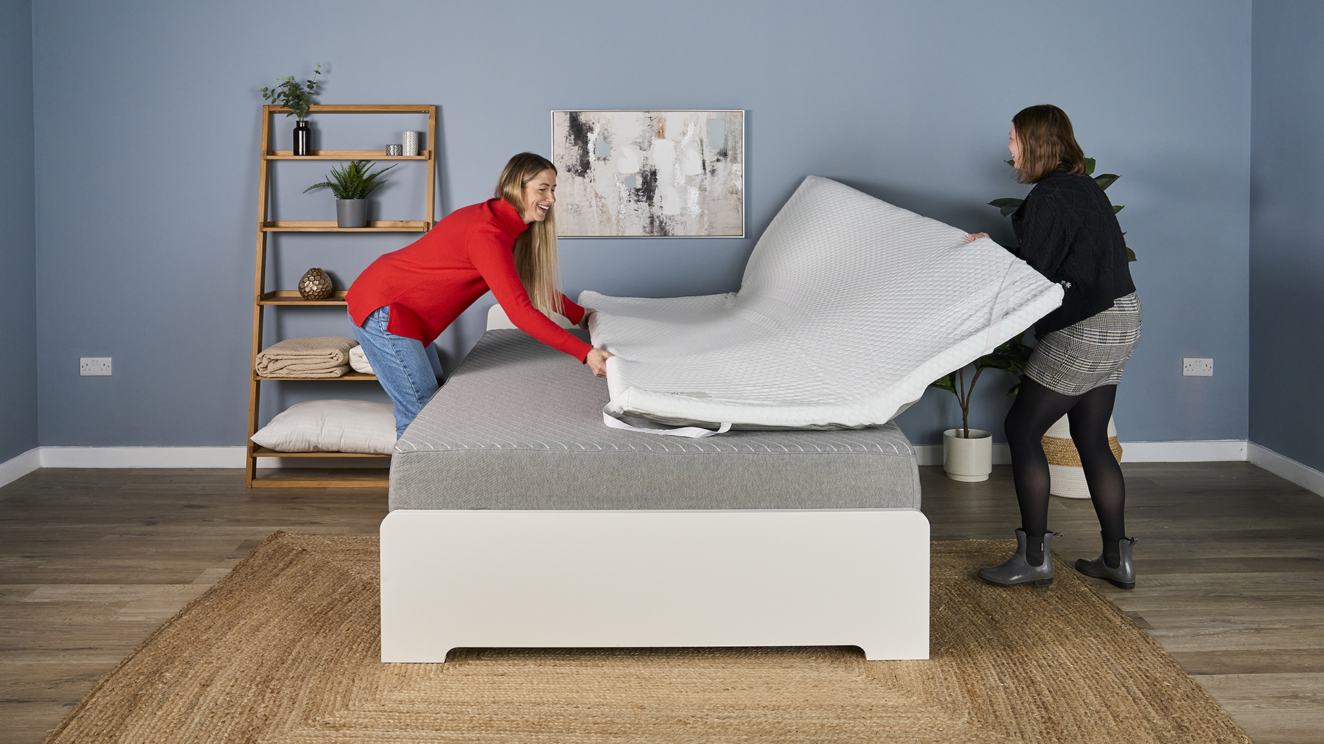 Testers unfold the unboxed Helix Dual Comfort Mattress Topper on a bed. 