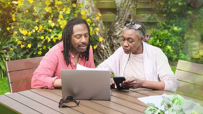 An older couple sit outside on their deck and look at a laptop together.