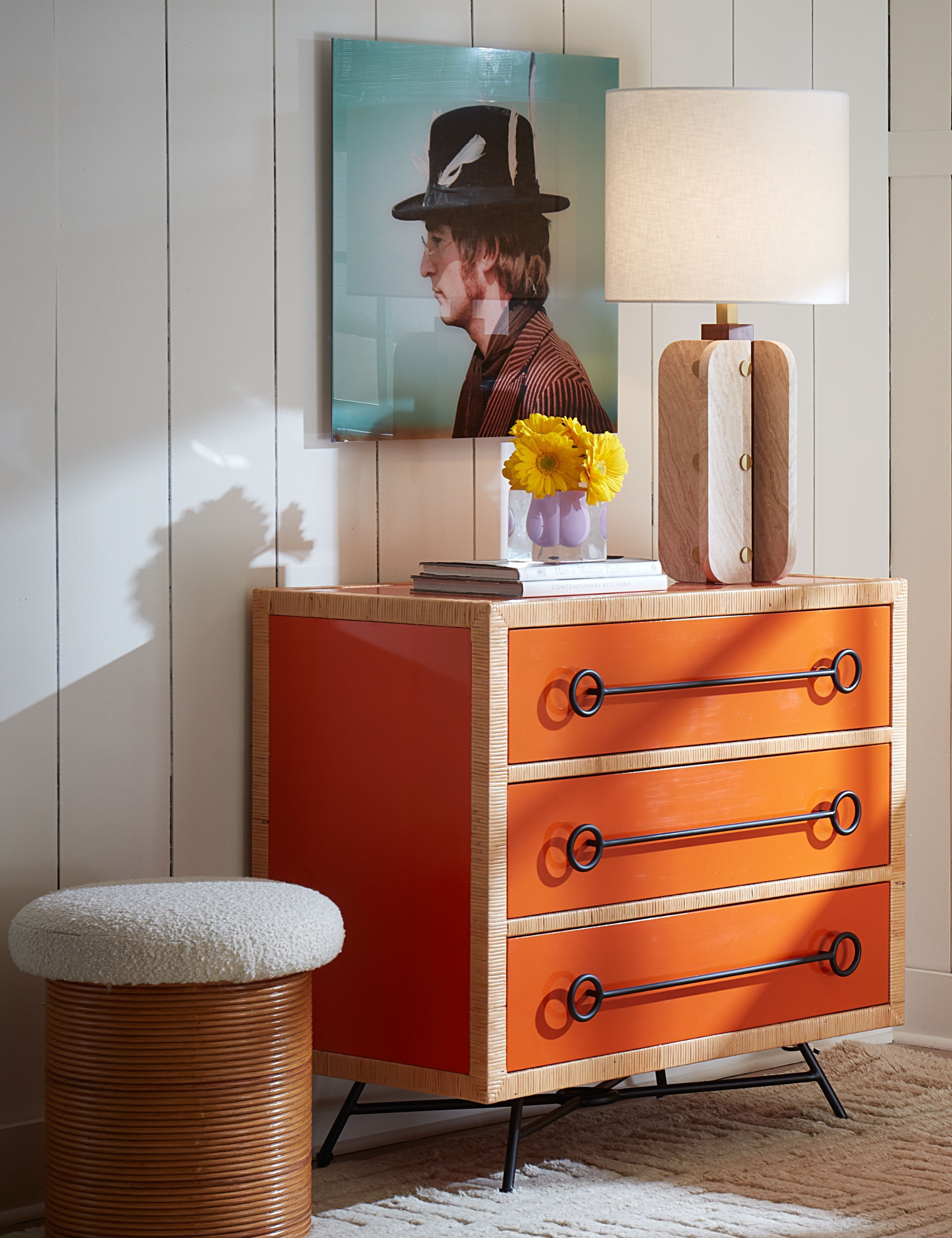 Orange lacquer chest styled inside of a white living room alongside a boucle topped wooden ottoman and oversized wooden table lamp