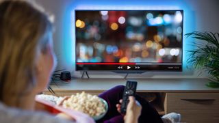 Woman watching a streaming program on her television while holding remote and popcorn.