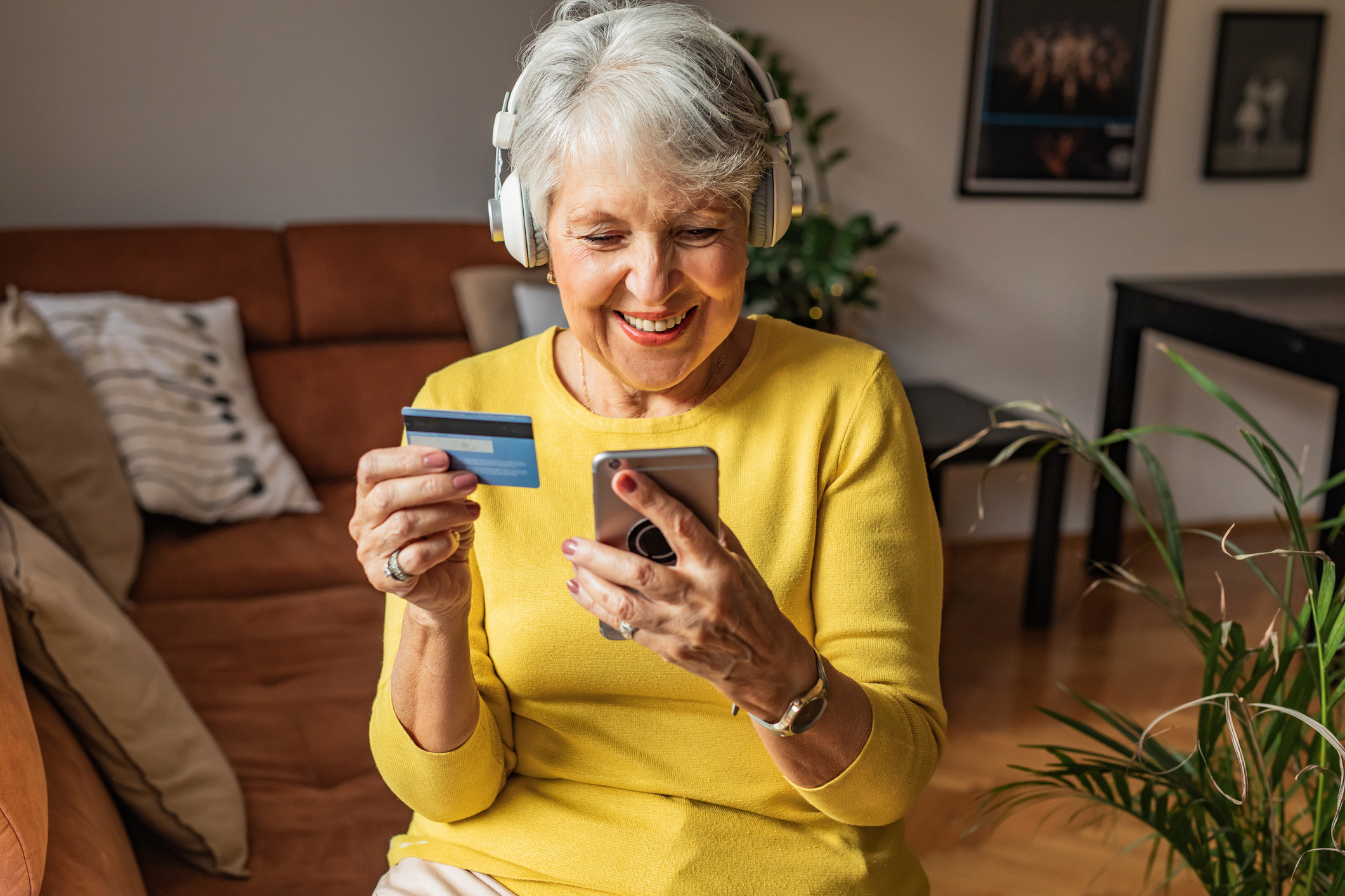 Happy senior woman at home, using smart phone and holding a credit card