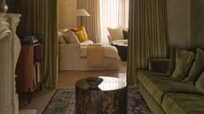 A green, moody color-drenched room with limewash walls, green curtains, green velvet sofa, and a white fireplace in view.
