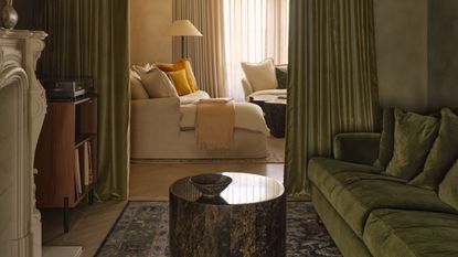 A green, moody color-drenched room with limewash walls, green curtains, green velvet sofa, and a white fireplace in view.