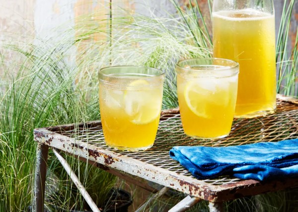 two glasses and a flip-top bottle filled with yellow liquid. set on a patio with greenery
