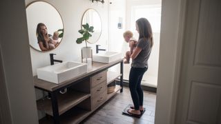 Best bathroom scales: A woman uses a smart scale in her bathroom to measure her body weight while holing her baby