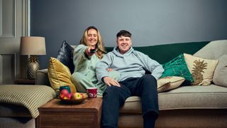 Gogglebox couple Roisin and Joe sitting on a smart cream sofa with a green throw on it.