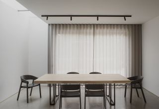 Minimalist dining area with soft curtain at Claygate house in Surrey
