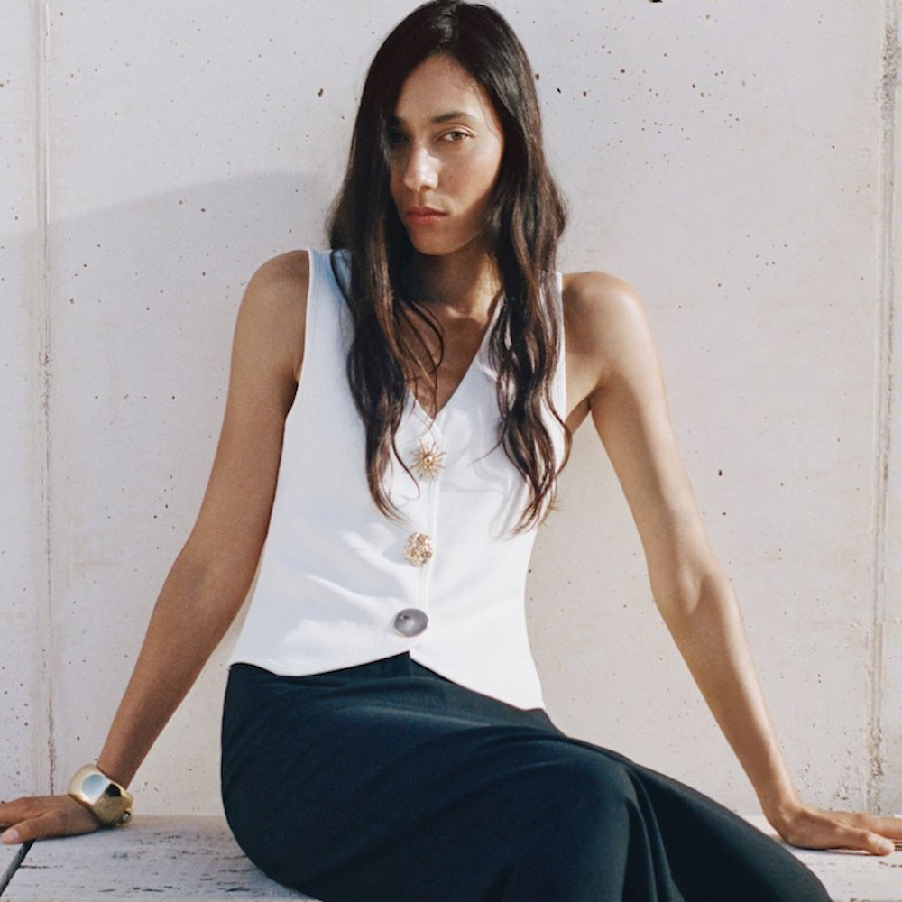 A model posing on a concrete seat wearing a white vest blouse and navy blue long pencil skirt from Mango