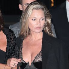 Kate Moss attending the Gucci show at the Tate Modern in London wearing a gray Gucci lingerie mini dress and a black coat with tights and Gucci slingback heels.