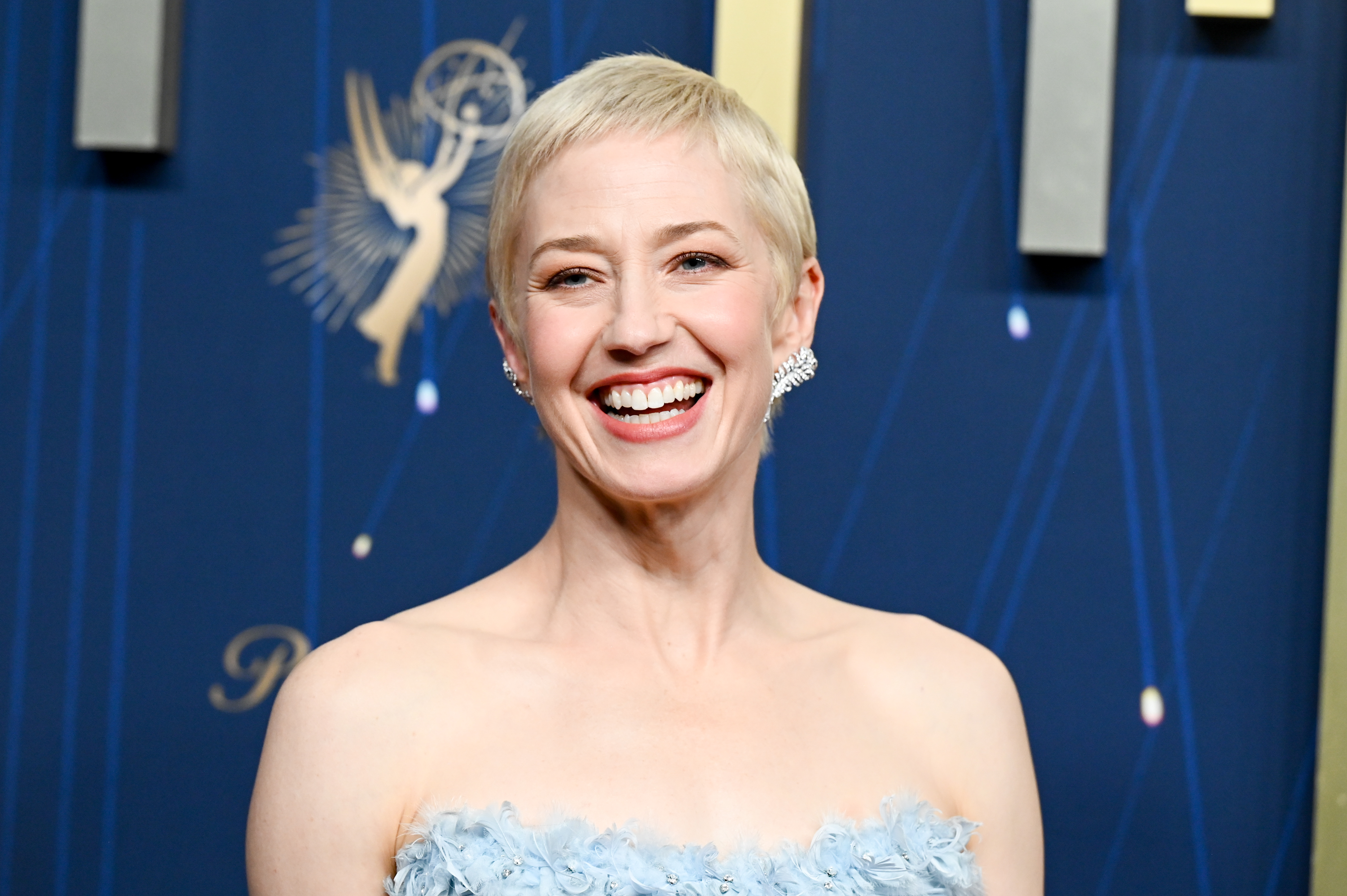 a woman with short, blonde hair smiling in front of a blue background