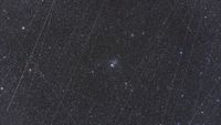 telescope photo of a star cluster in a dark night sky, with white streaks caused by satellites all over the image