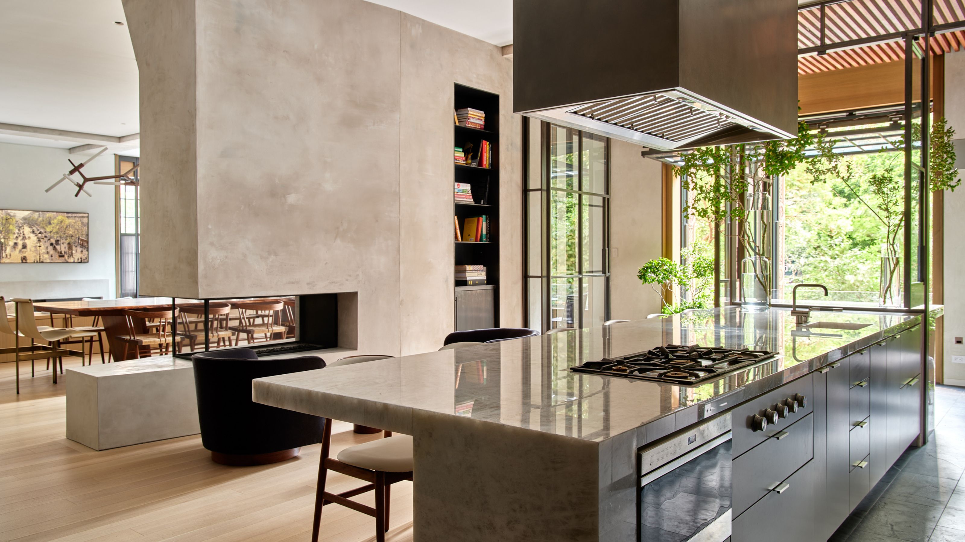 Large open plan kitchen with dark modern cabinets and a large stone islands with seating and plaster wall to separate the dining space