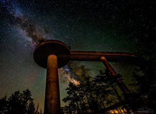 The Milky Way streaks by behind a tall, curving observation tower.