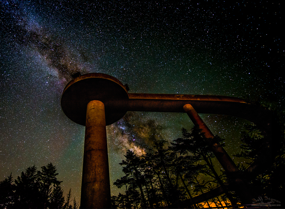 The Milky Way streaks by behind a tall, curving observation tower.