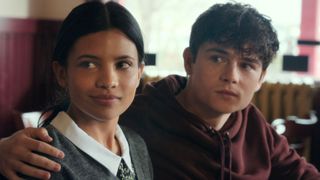 Alex has his arm around Jackie as they look at something offscreen