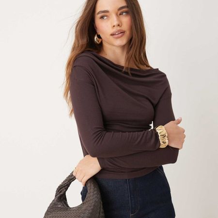 Woman wears brown draped top, gold bracelet and blue jeans