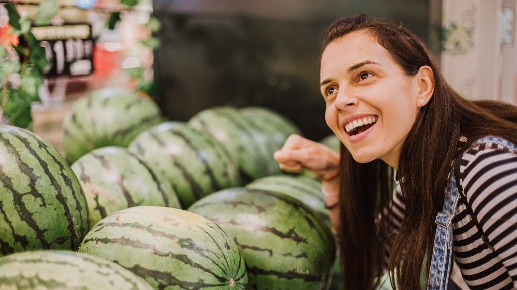 A woman listens as she knocks on a ripe watermelon with her fist