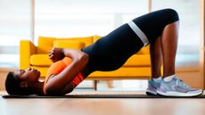 Woman in bridge position with resistance band around her legs, a yellow sofa is behind her