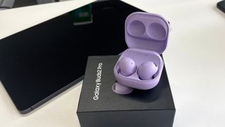 Galaxy Buds 2 Pro in charging case, in purple with packing box and Samsung tablet in background