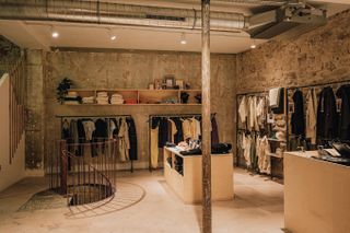 A warmly lit concept store is filled with home accessories and fashion garments and characterized by an industrial setting.