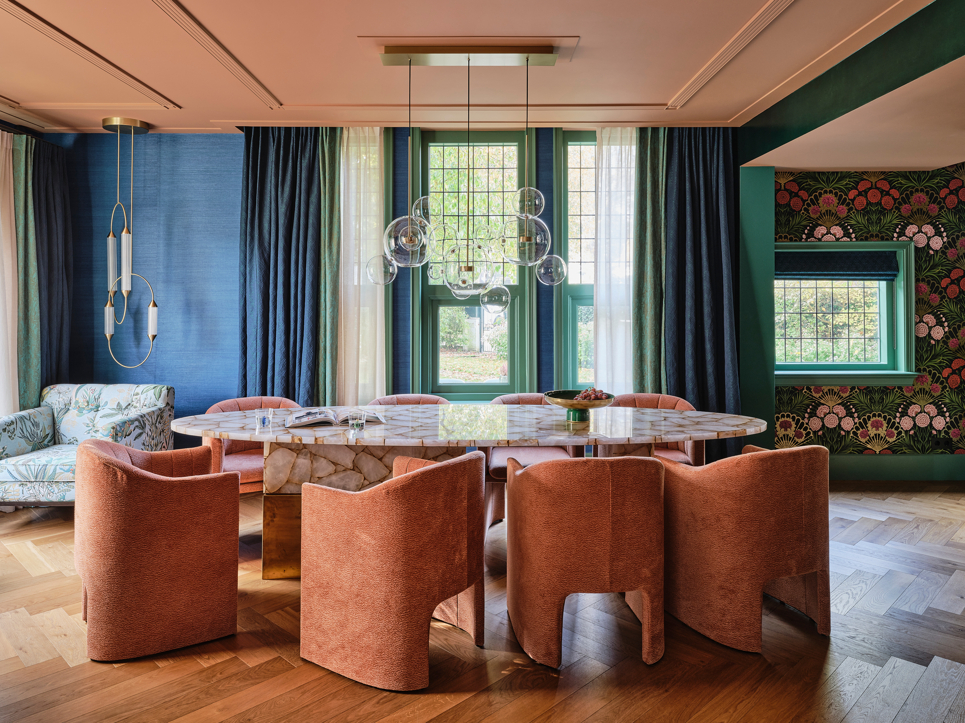 Dining room with marble table, coral chairs, pink ceiling, green and blue walls, and globe chandelier