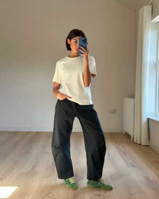 Marianne wears a white t-shirt, black wash barrel-leg jeans, and green Dries Van Noten sneakers.