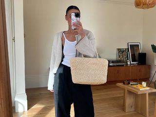 Emily wore a white tank top and cardigan over dark pants, and strappy sandals while carrying a straw tote bag.
