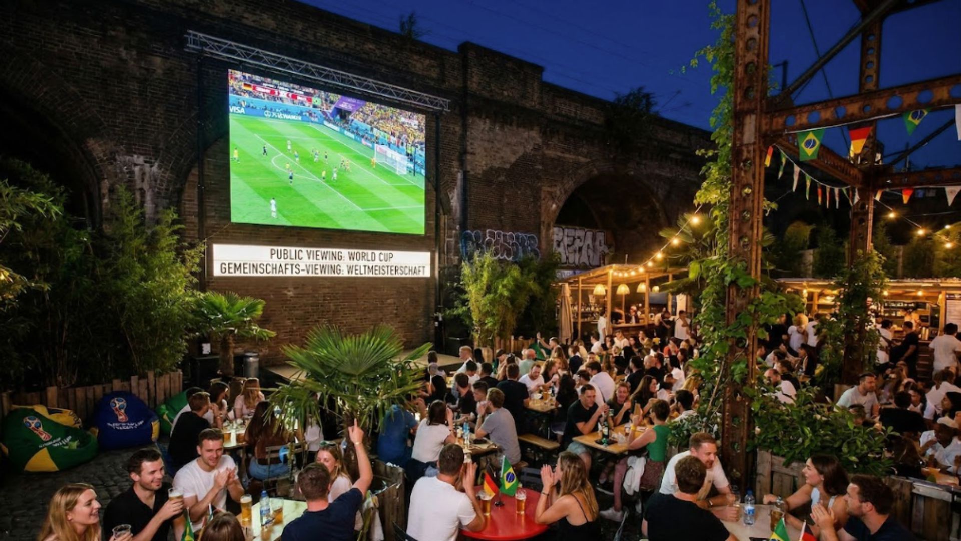 an artist rendering of what the german kraft brewery will look like with the screen playing a world cup match and people gathered around on benches