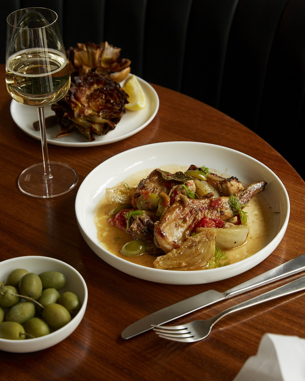 An appetising meal of chicken, artichokes, and olives, paired with white wine, captured from above on a wooden table.