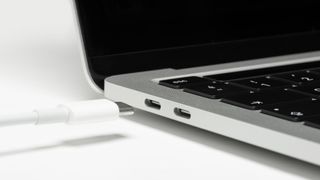 A side view of a laptop showing two USB Type C ports and a white USB C cable about to be plugged in