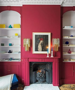 Living room with bright pink walls and elaborate white cornice, cupboards and shelving built into either side of the chimney breast and fireplace
