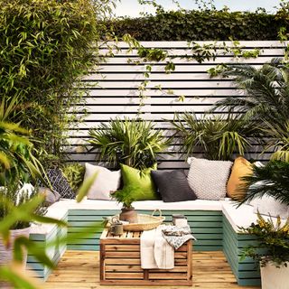 small garden with compact seating idea on decking. White painted fence, wooden coffee table, cushions, plants