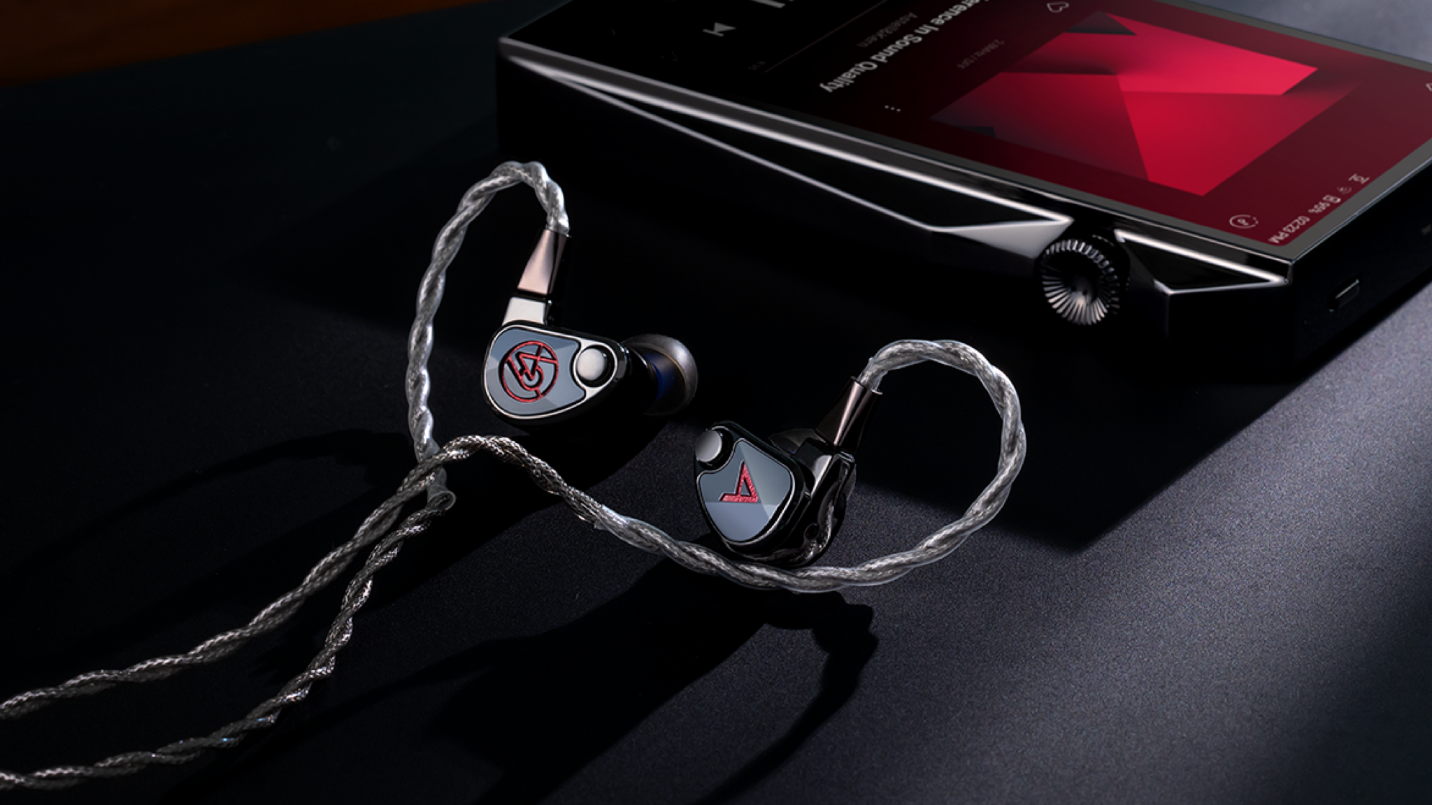 The Astell &amp; Kern XIO in-ear monitors sitting on a dark surface beside an Astell &amp; Kern hi-res audio player
