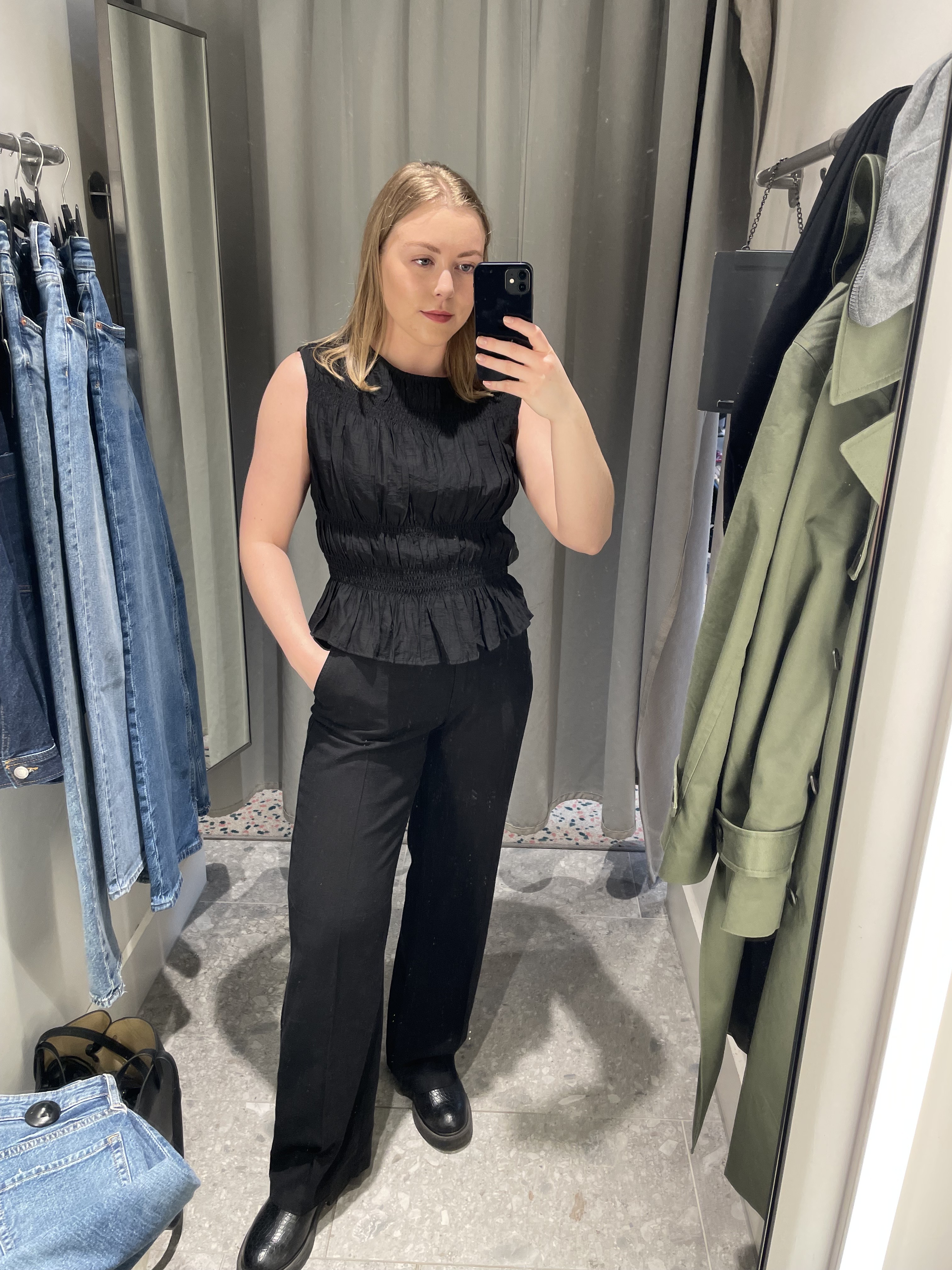 Woman in dressing room wears black top black linen trousers and boots