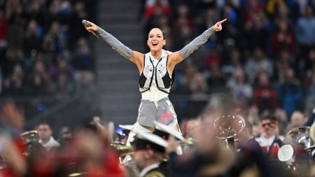 Singer Katy Perry points with arms raised pointing to a crowd over a marching band