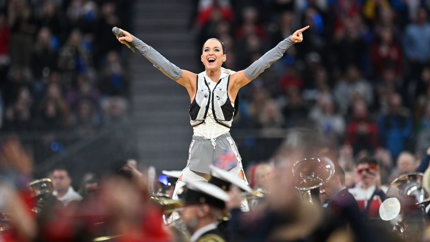 Singer Katy Perry points with arms raised pointing to a crowd over a marching band