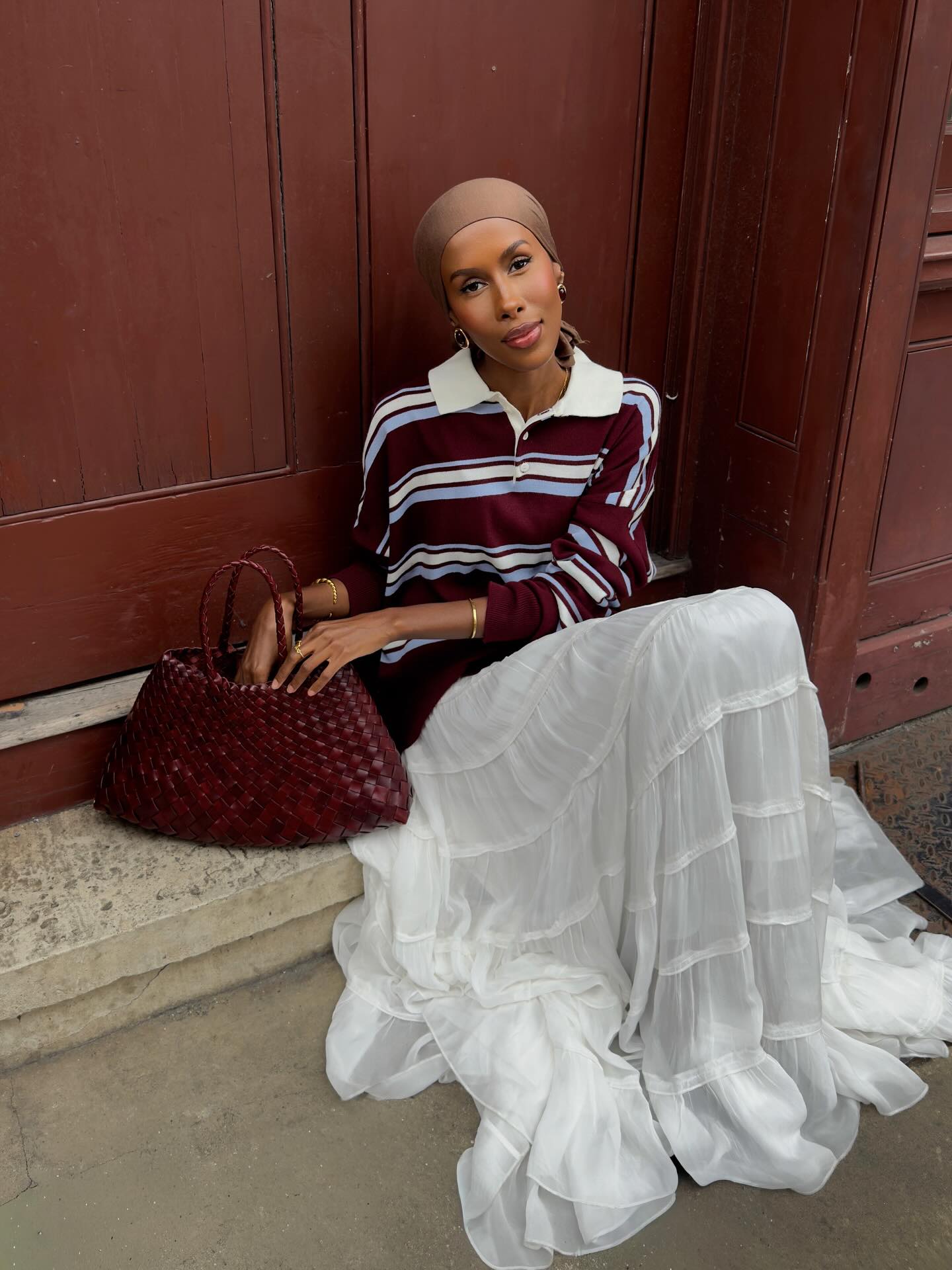 A woman sitting on a doorstep wearing a white skirt and berry-coloured top with a berry-toned makeup look