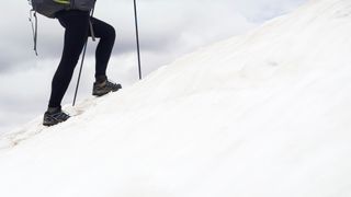 A hiker's legs climbing a steep, snowy slope