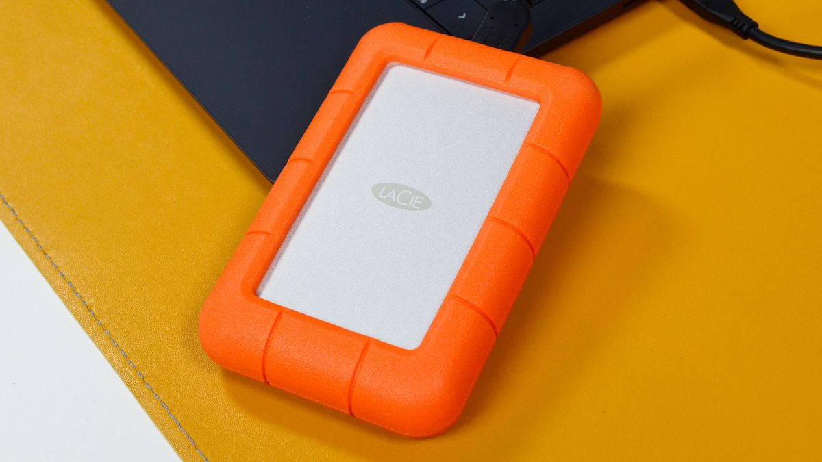 A LaCie Rugged Mini external hard drive on a desk with a laptop